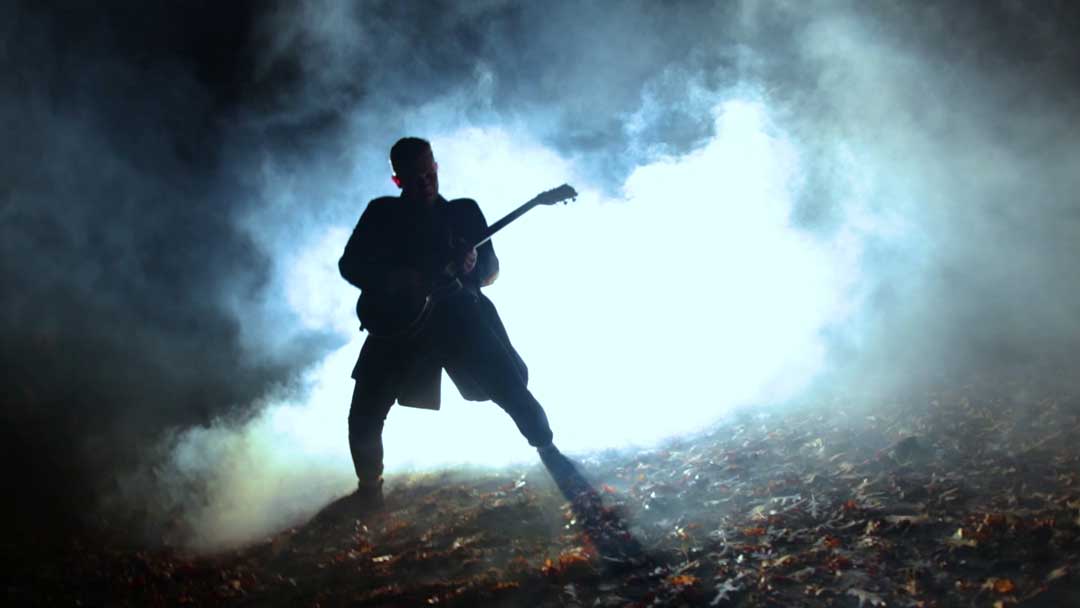 Ein Mann mit Gitarre nachts im Nebel im Wald